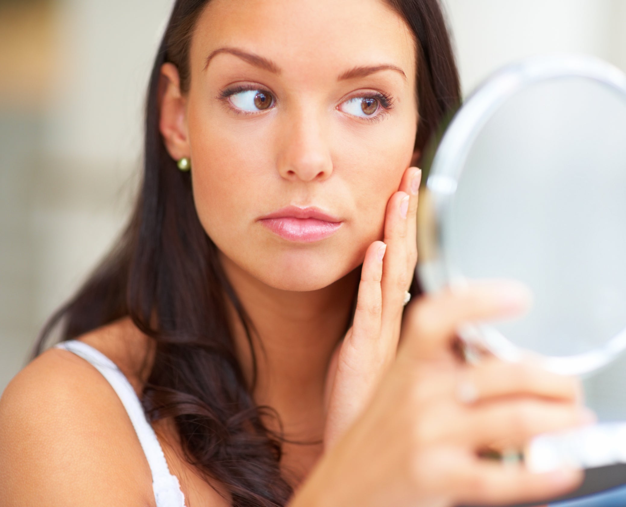 Woman looks at her skin in a mirror.